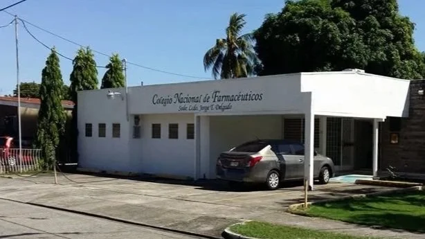 Edificio de un colegio llamado Colegio Nacional de Farmacéuticos con un coche estacionado en la entrada y árboles en el fondo.