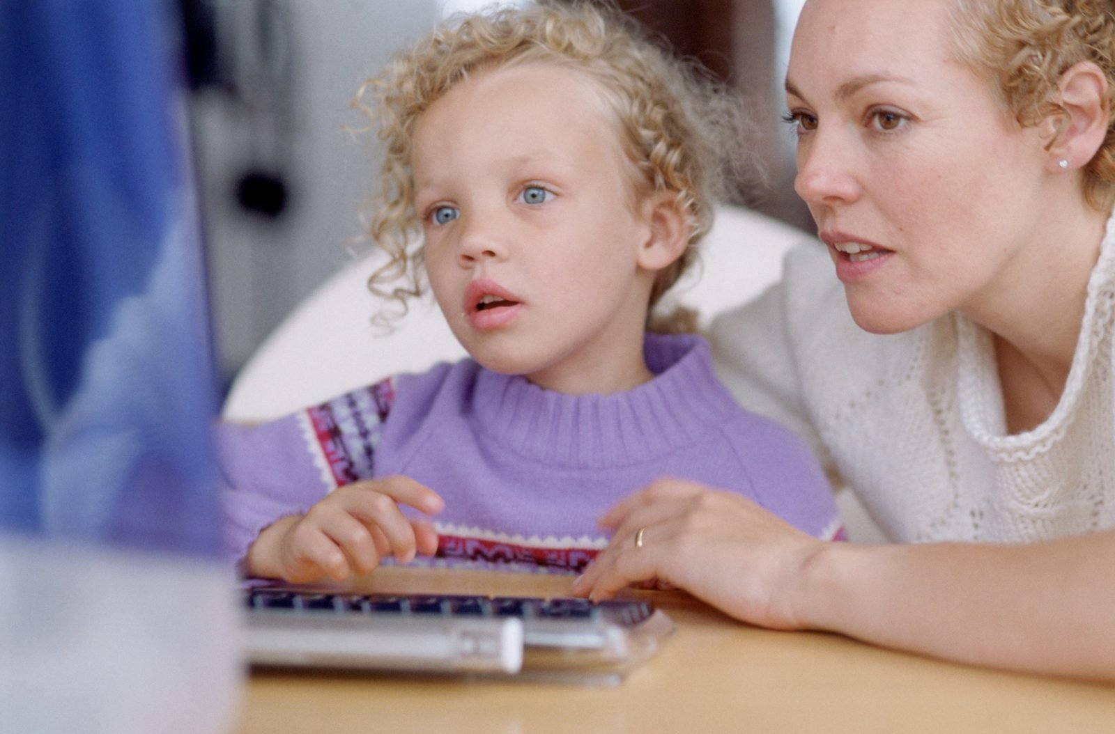 A mother and her young daughter looking at a laptop screen together