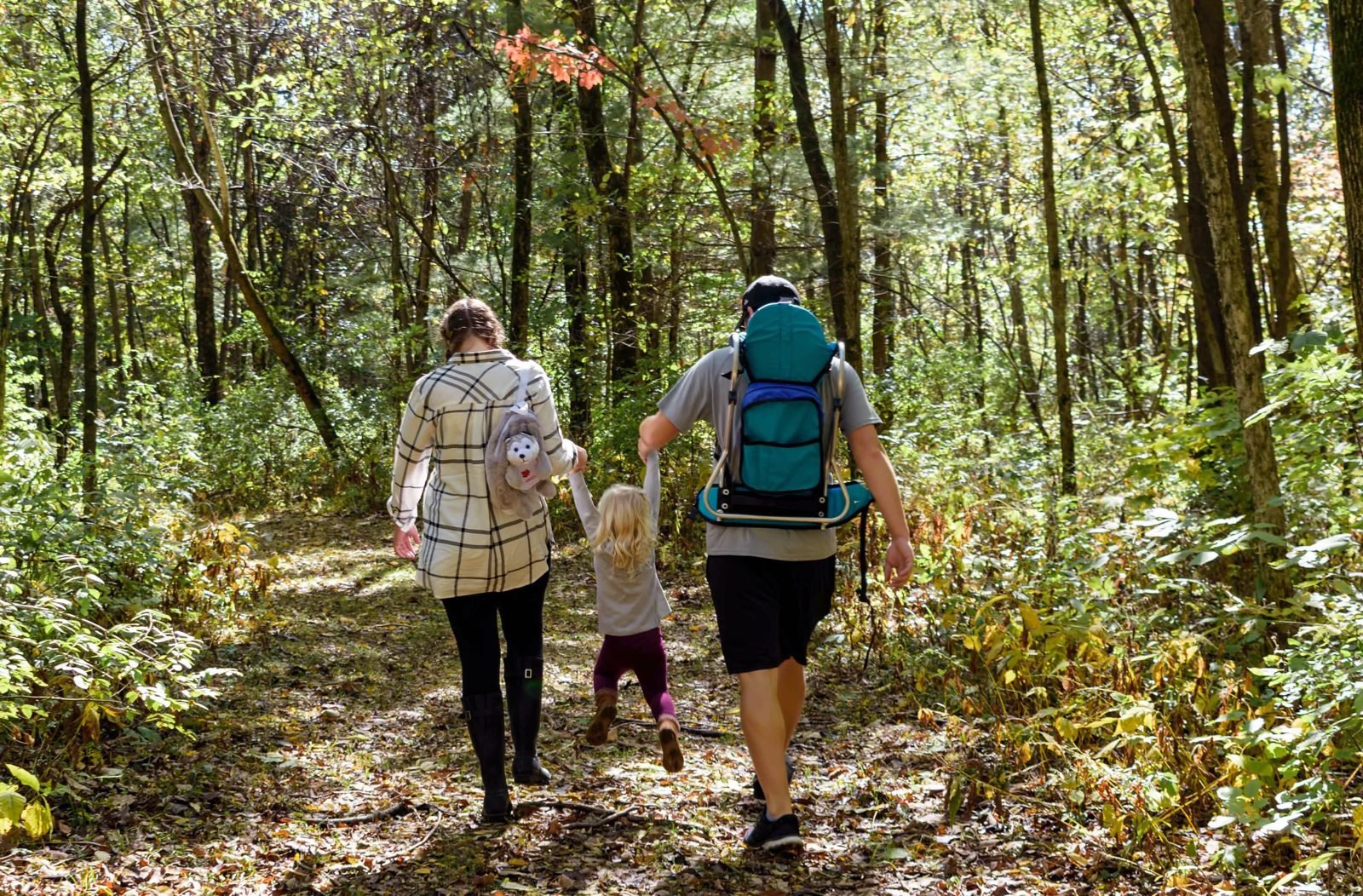 Parents swinging their young daughter between them on a wooded trail