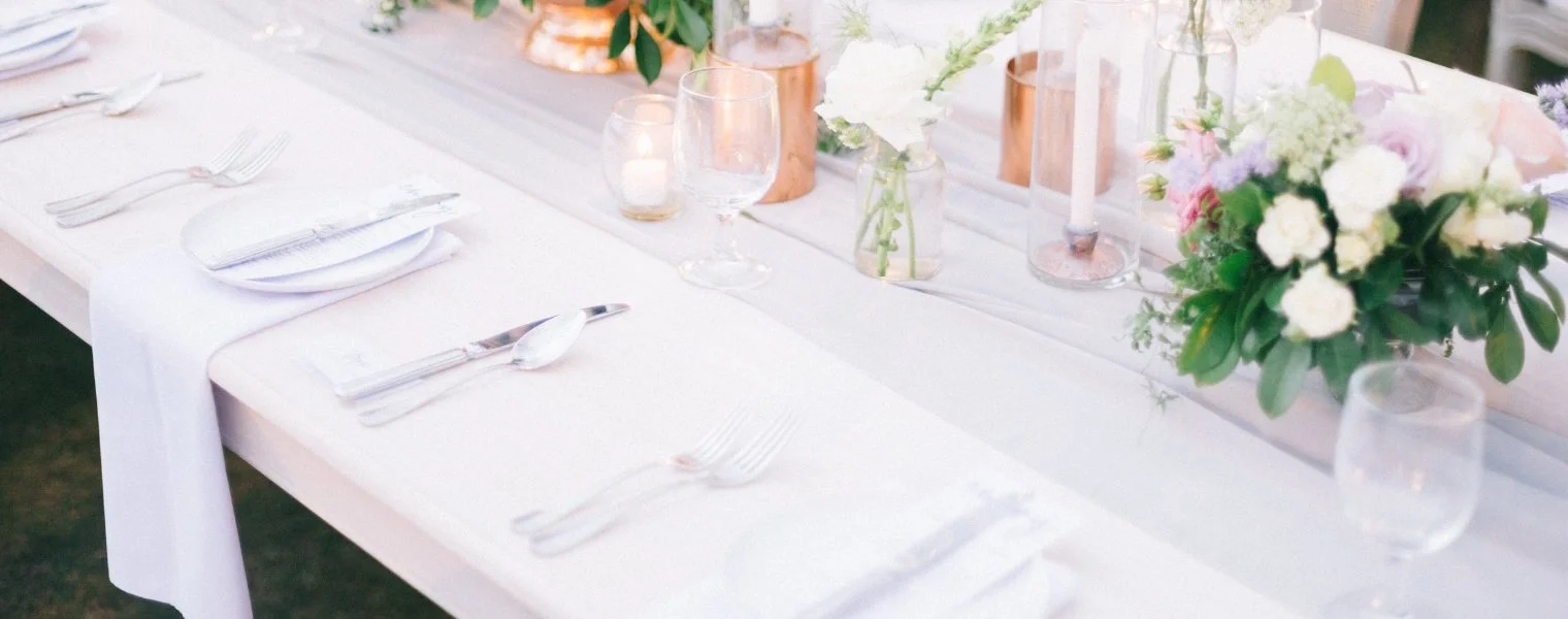 A decorated table set for a formal event with white linens, flower arrangements, candles, and glassware.