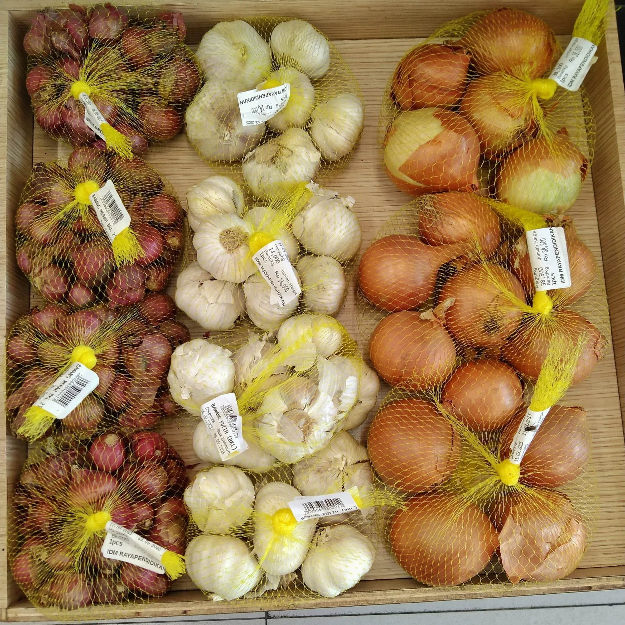 Bags of red onions, garlic, and yellow onions display in a wooden crate.