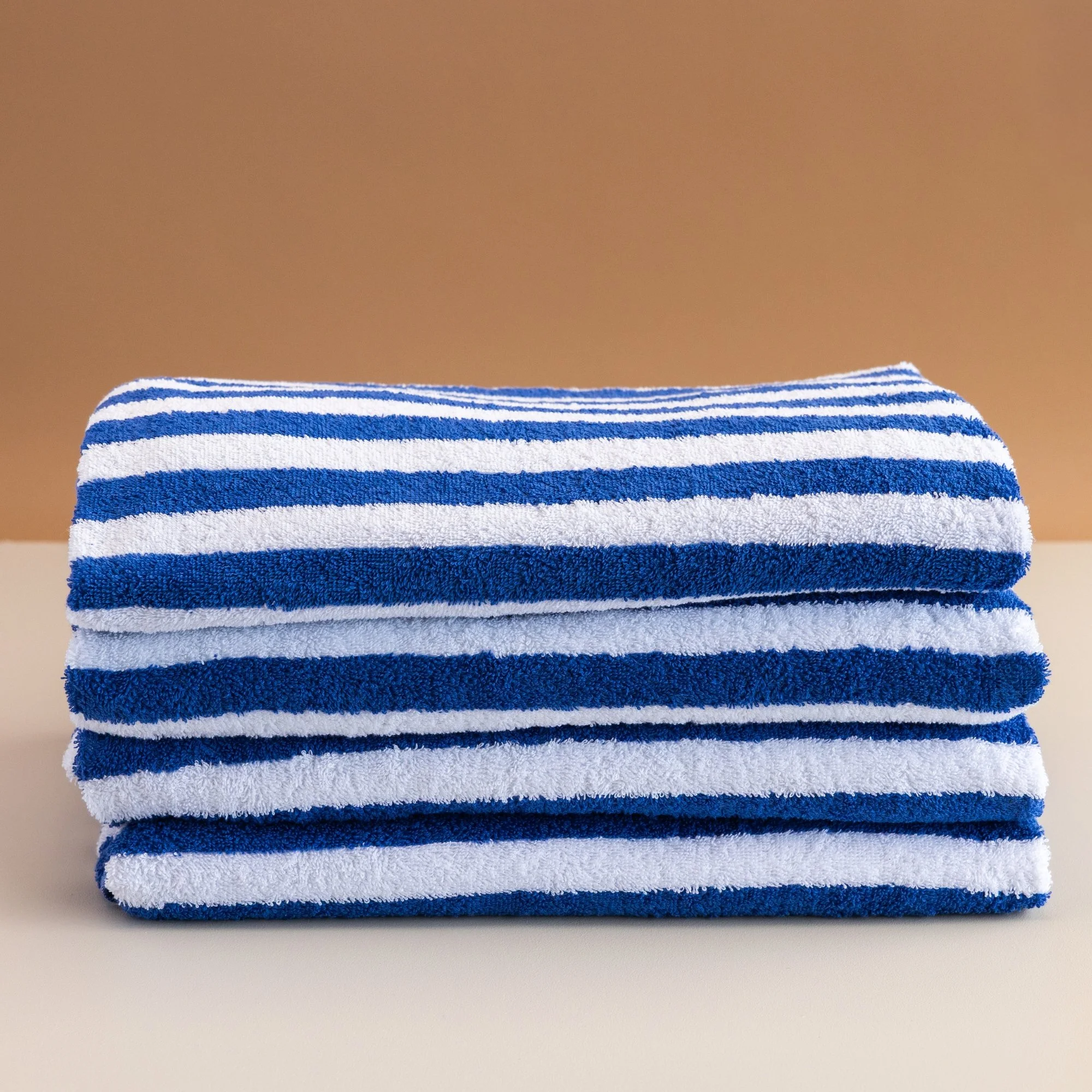 Stack of  Tasman blue and white striped pool  towels on a white surface against a beige background.