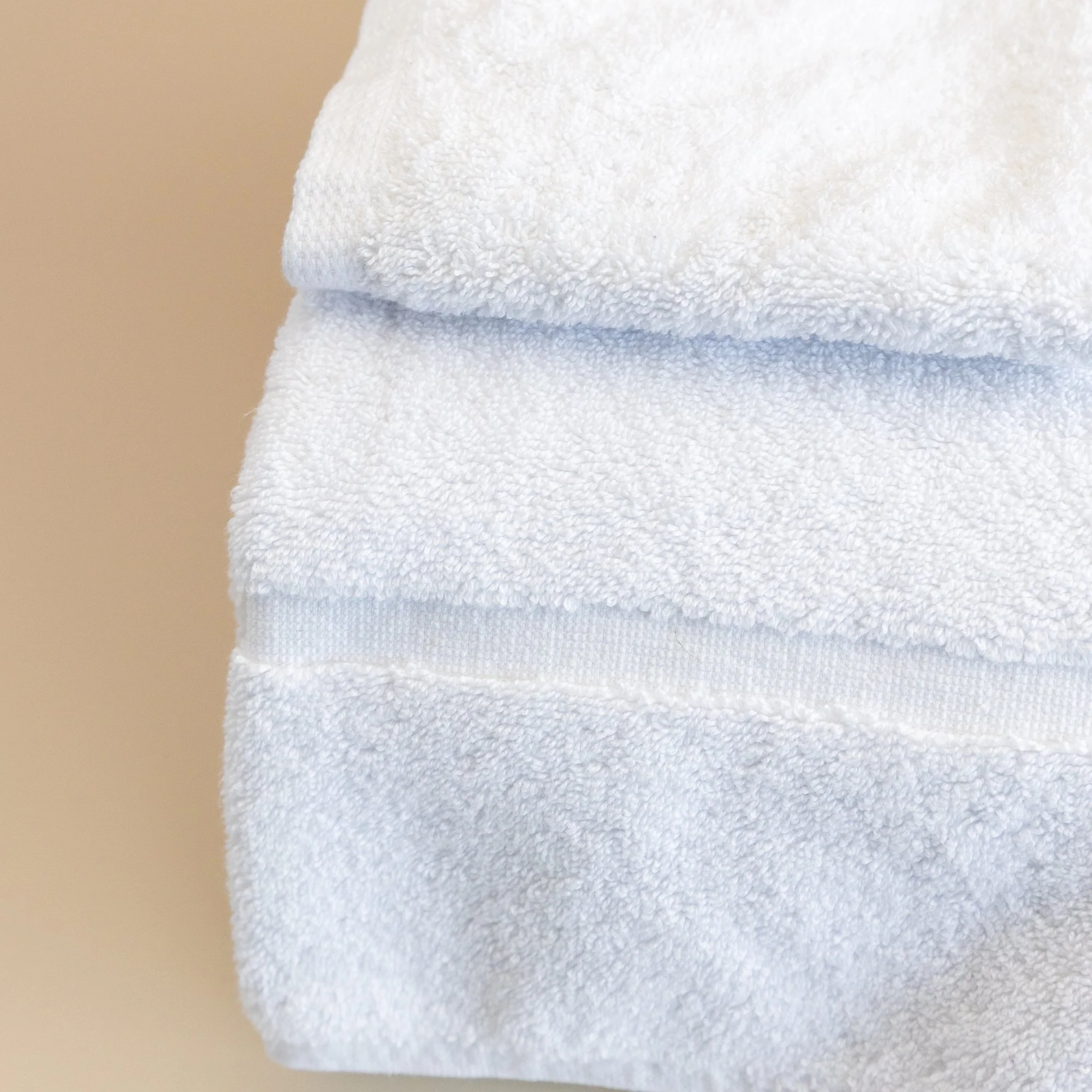Close-up of stacked Tasman white towels on a beige background.