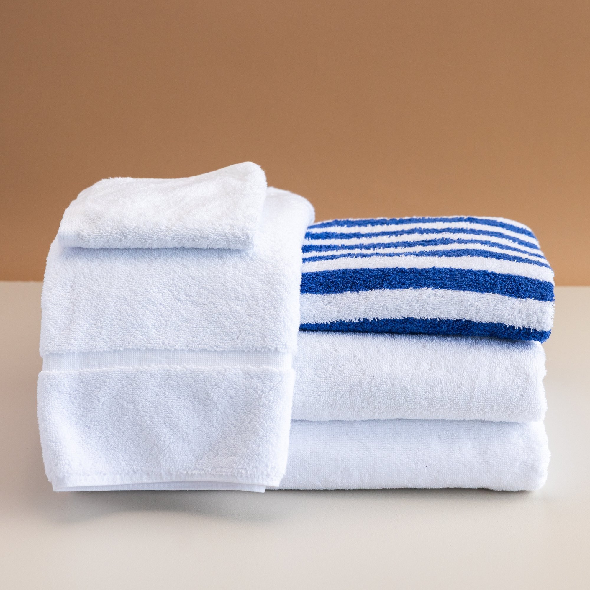 Stack of Tasman white and blue striped towels and white washcloths on a beige background.