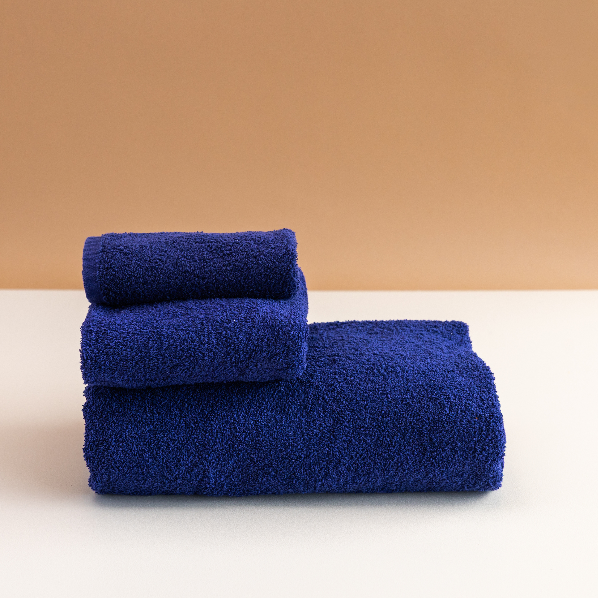 Three folded blue Kahurangi towels stacked on a white surface with a light brown background.