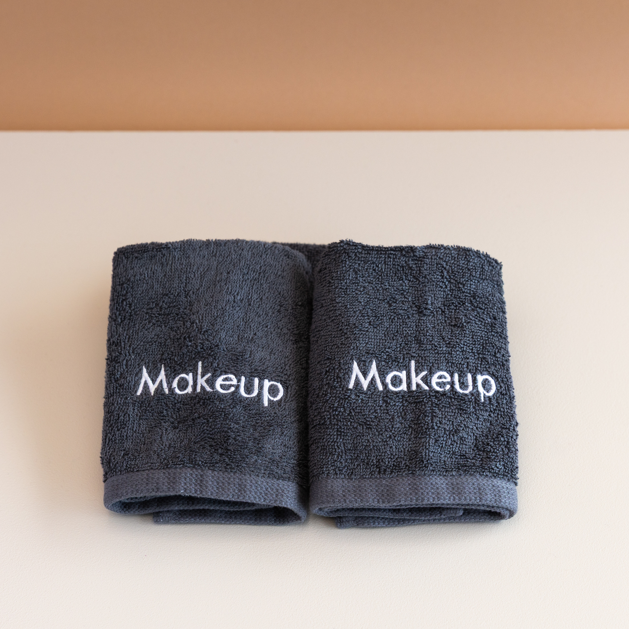 Two dark gray Kahurangi towels embroidered with the word 'Makeup' in white, placed on a white surface.