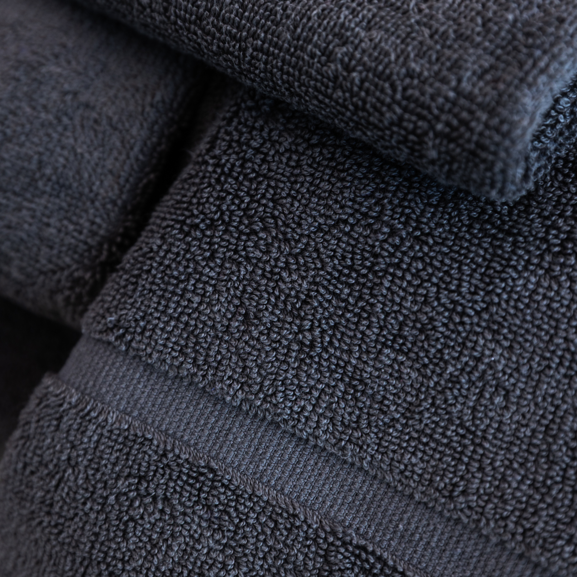 Close-up of a dark gray or black textured fabric, showing tight, looped knit pattern.