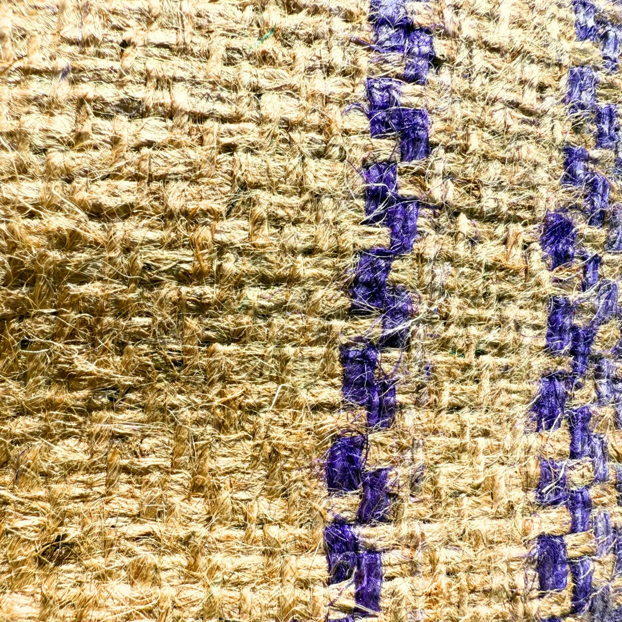 Close-up of a woven textile with gold-colored threads and vertical purple stripes.