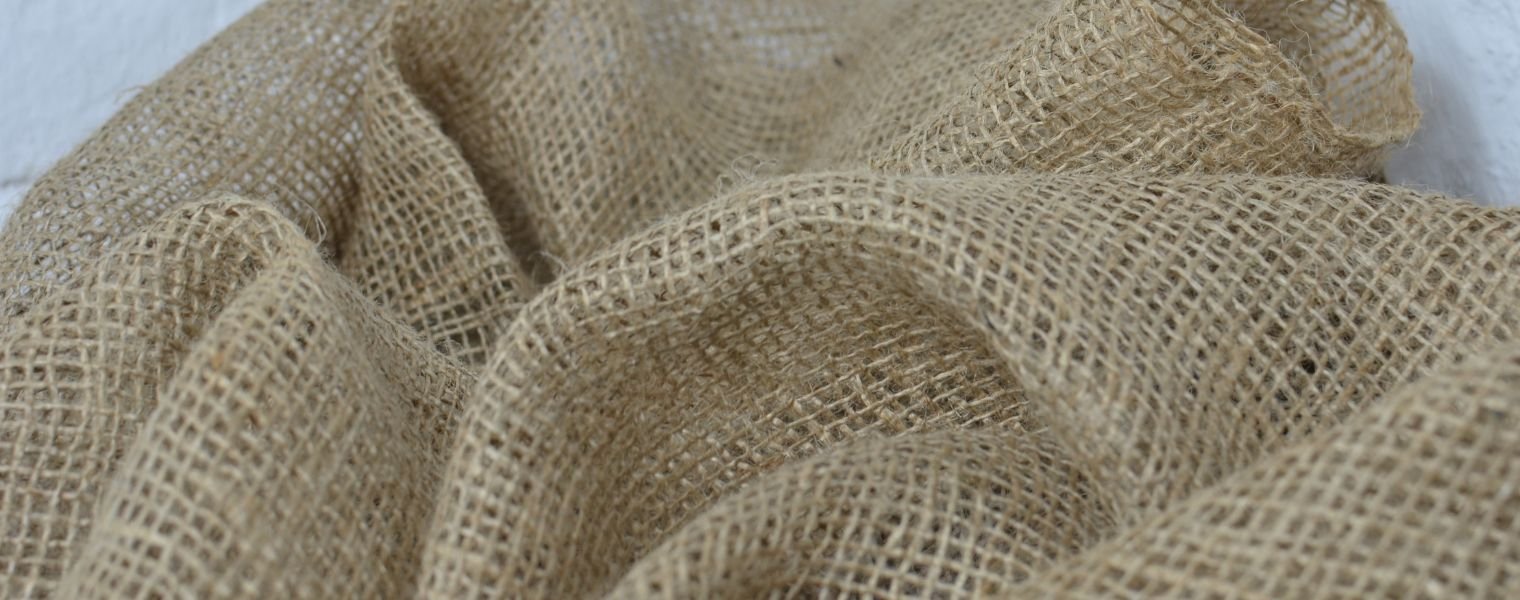 Close-up of beige burlap fabric with a rough woven texture, draped in folds.