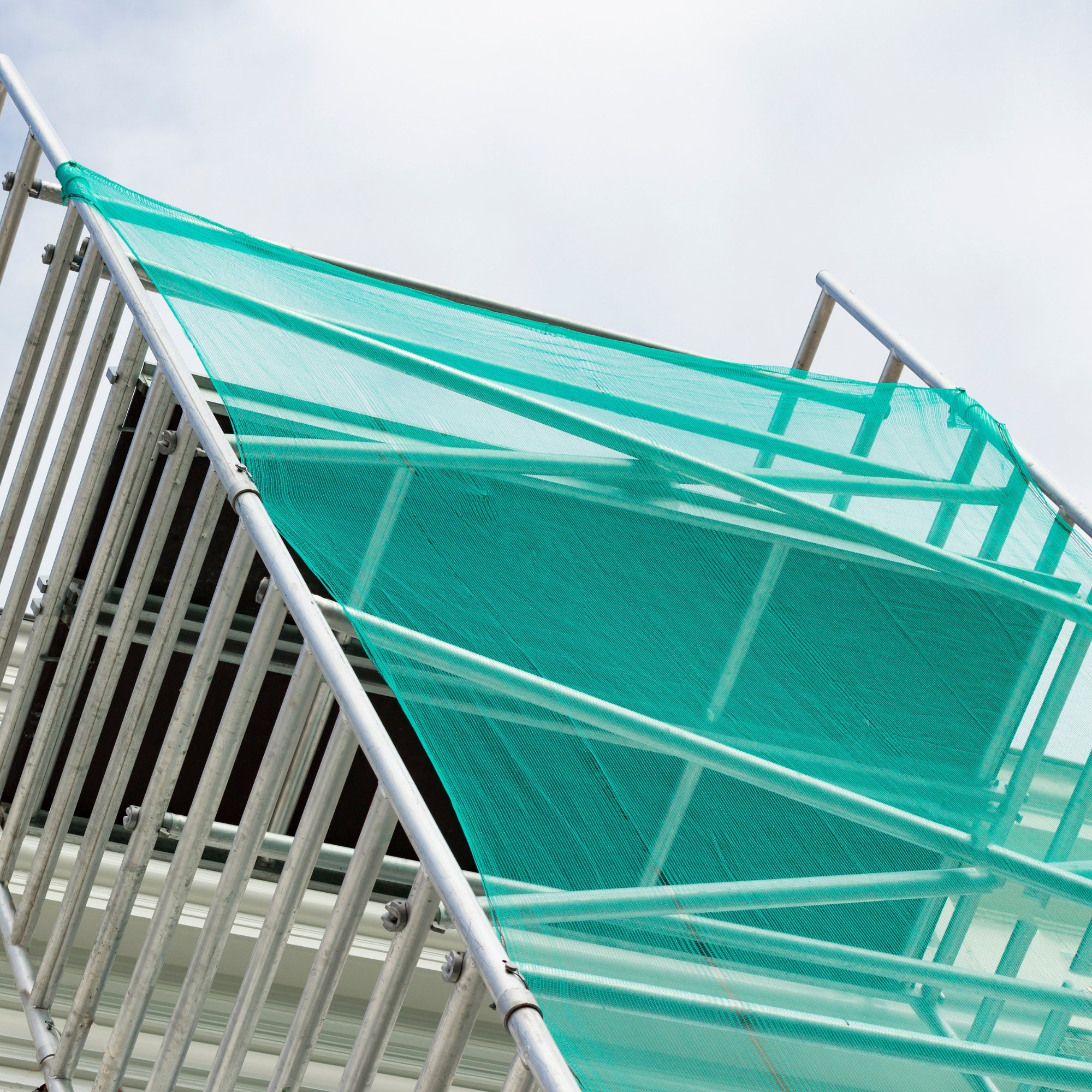 A close-up view of a metal scaffold with a green scaffold net.