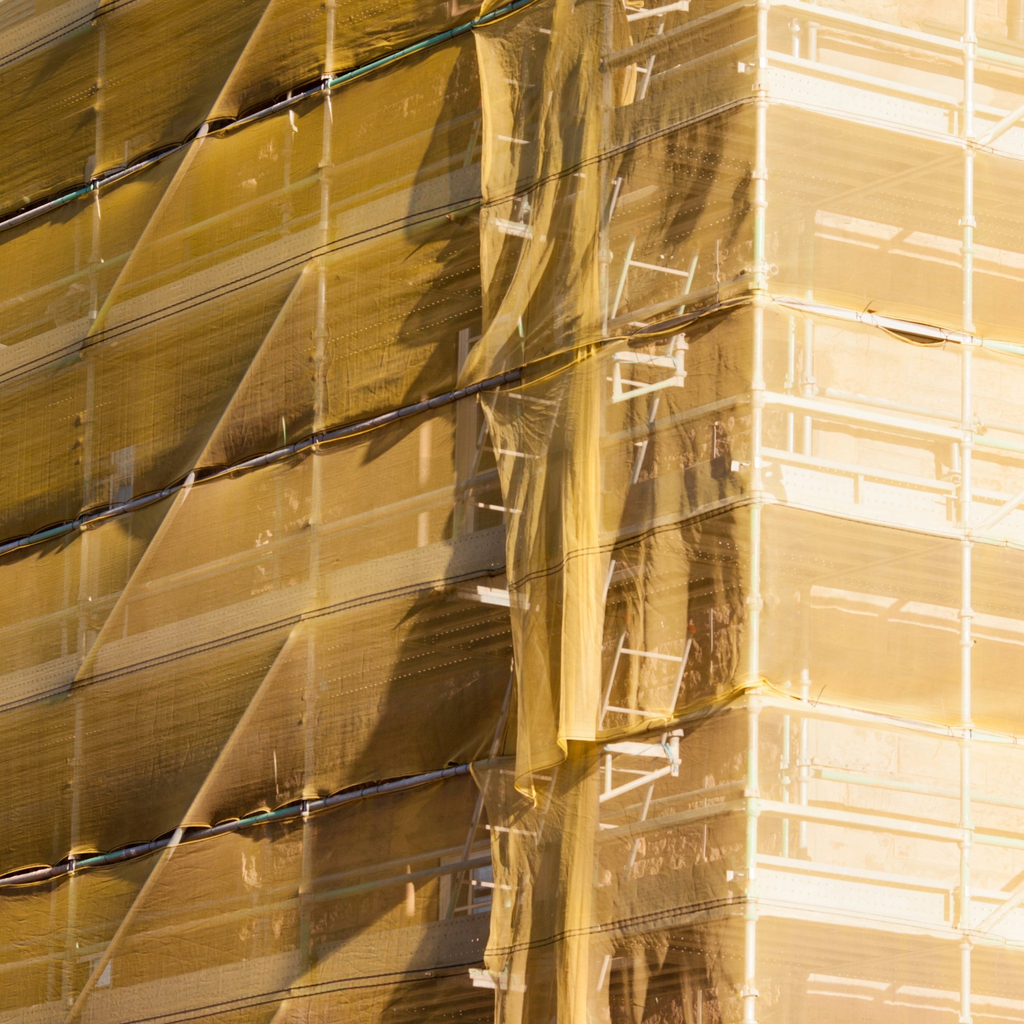 Building under construction wrapped in yellow scaffold netting.