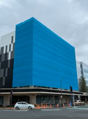Modern multi-story building with a blue scaffold net around it.