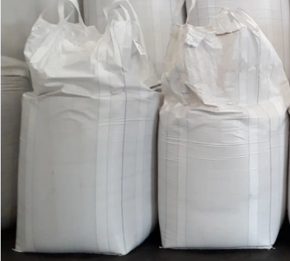 Two large white bags made of woven polypropylene material, filled and standing upright.