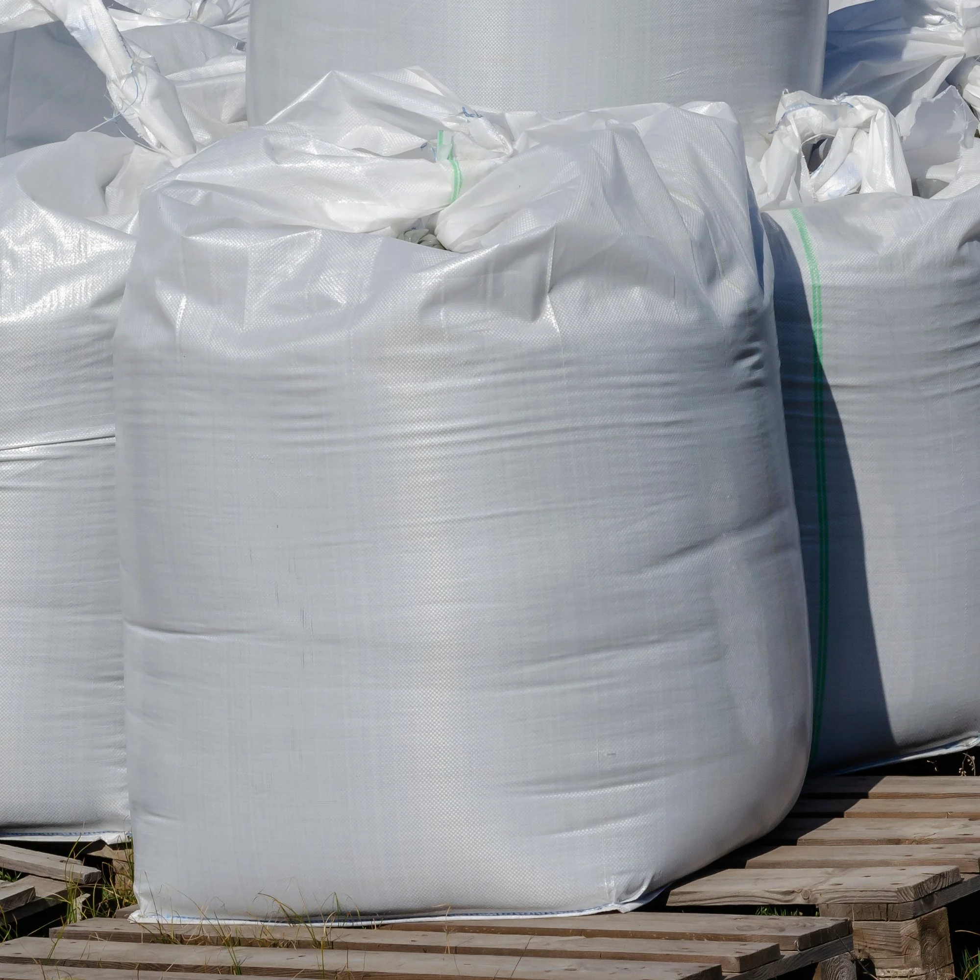 White FIBC bags on wooden pallets, filled with unknown material.