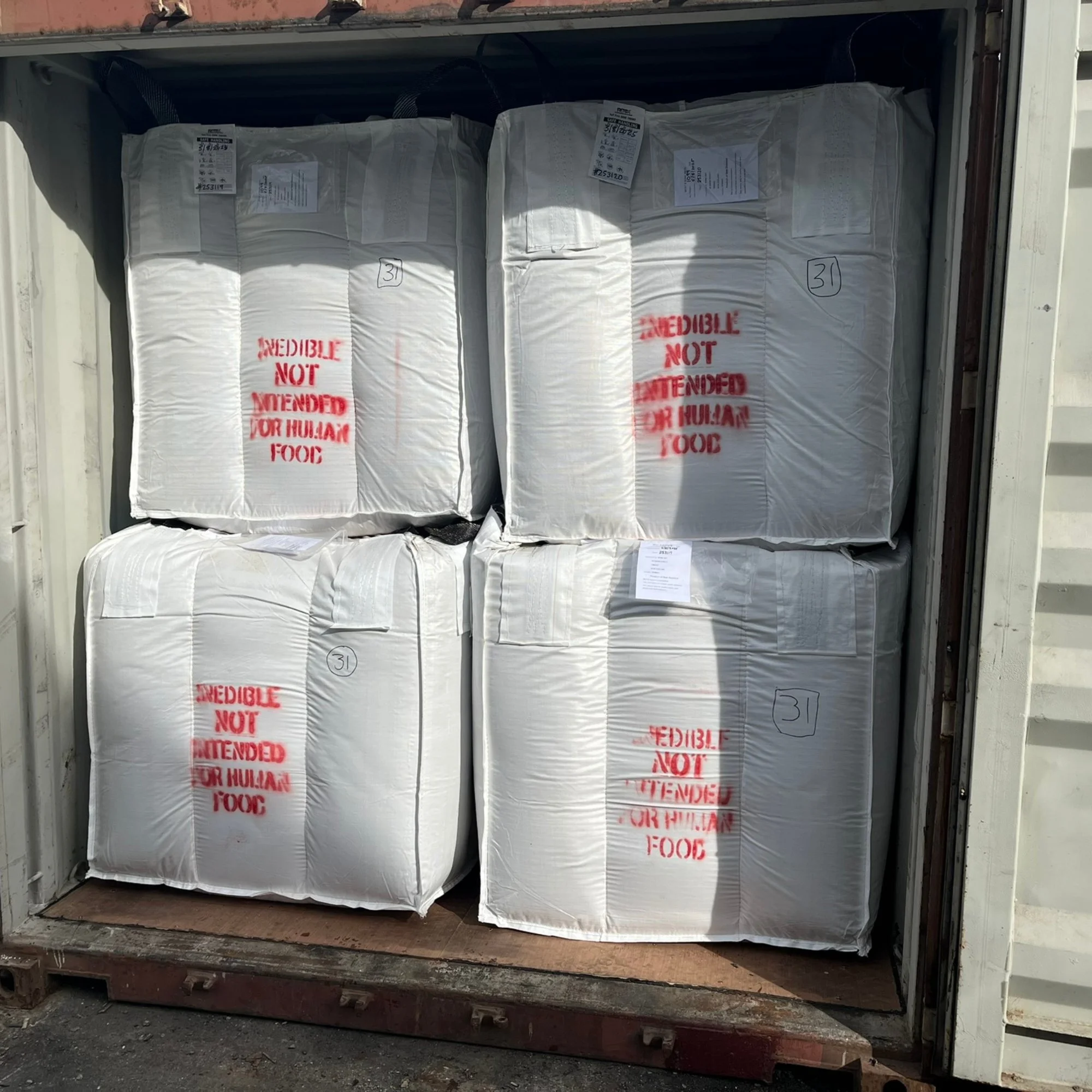 Four large FIBC baffle bags with red text stating 'EDIBLE NOT INTENDED FOR HUMAN FOOD' stacked inside a shipping container.