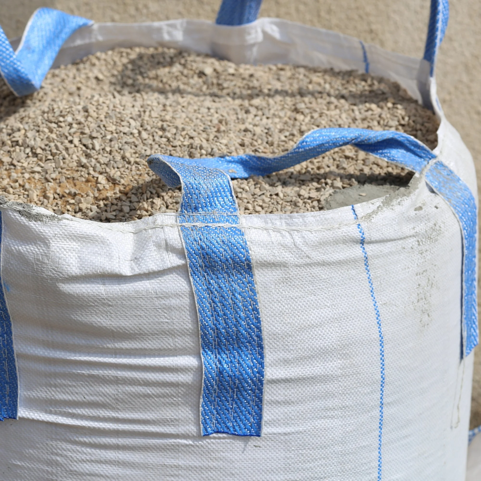 Large white and blue woven FIBC bag filled with gravel.