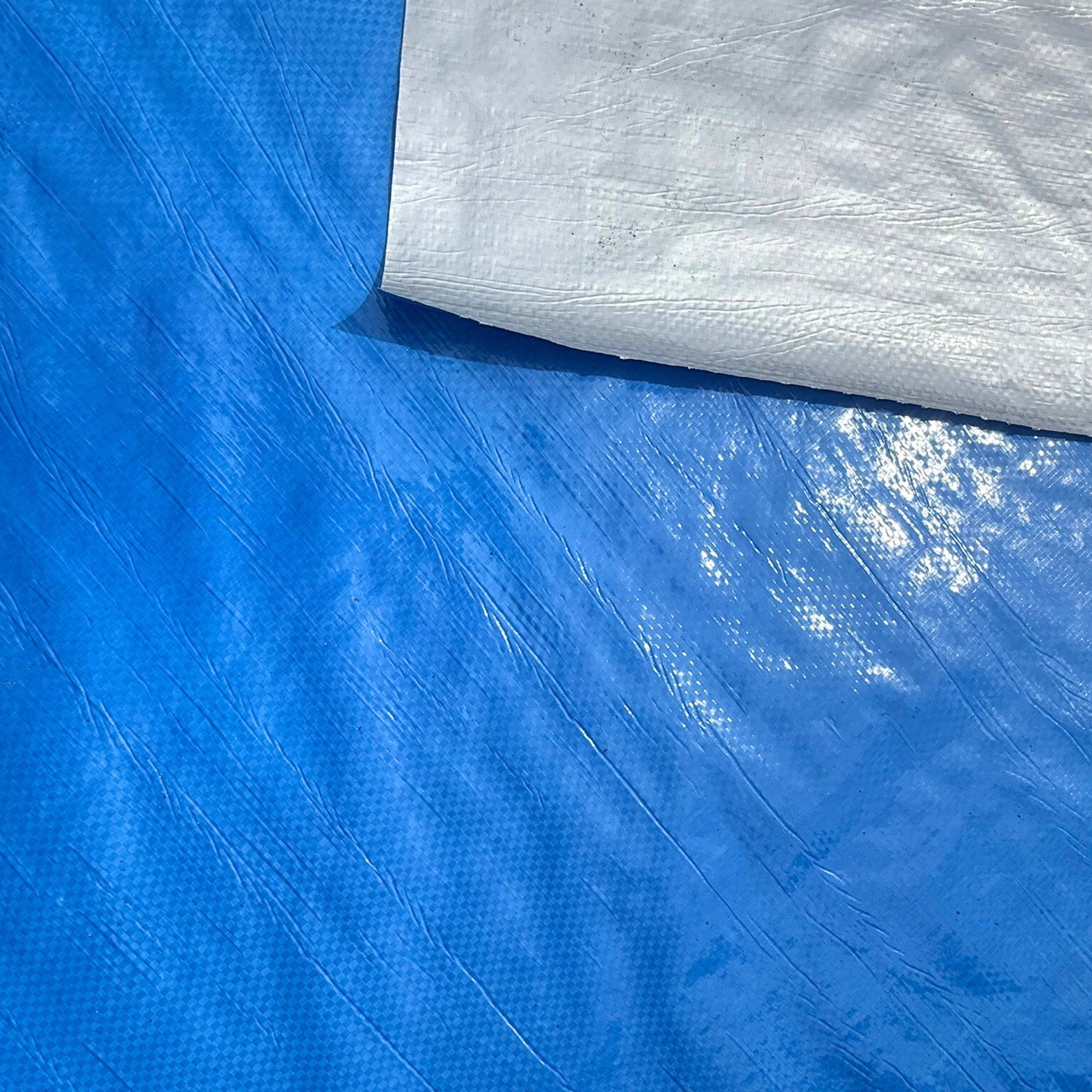 Close-up of a blue plastic tarp with a white textured fabric on top.
