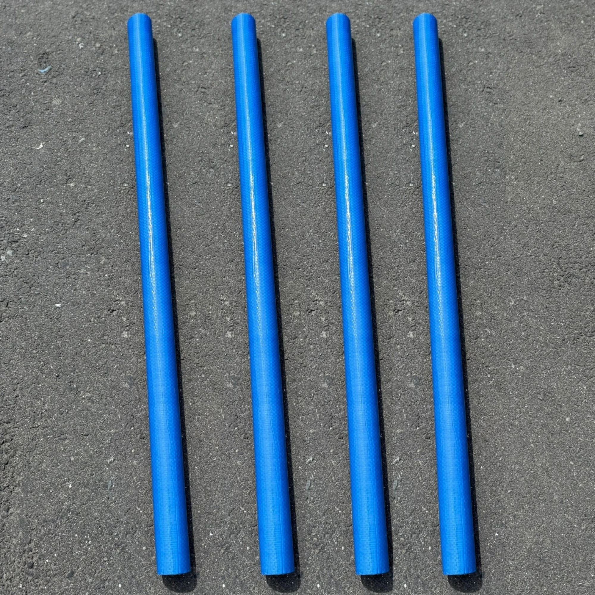 Four blue plastic golf club shafts lying parallel on a gray asphalt surface.