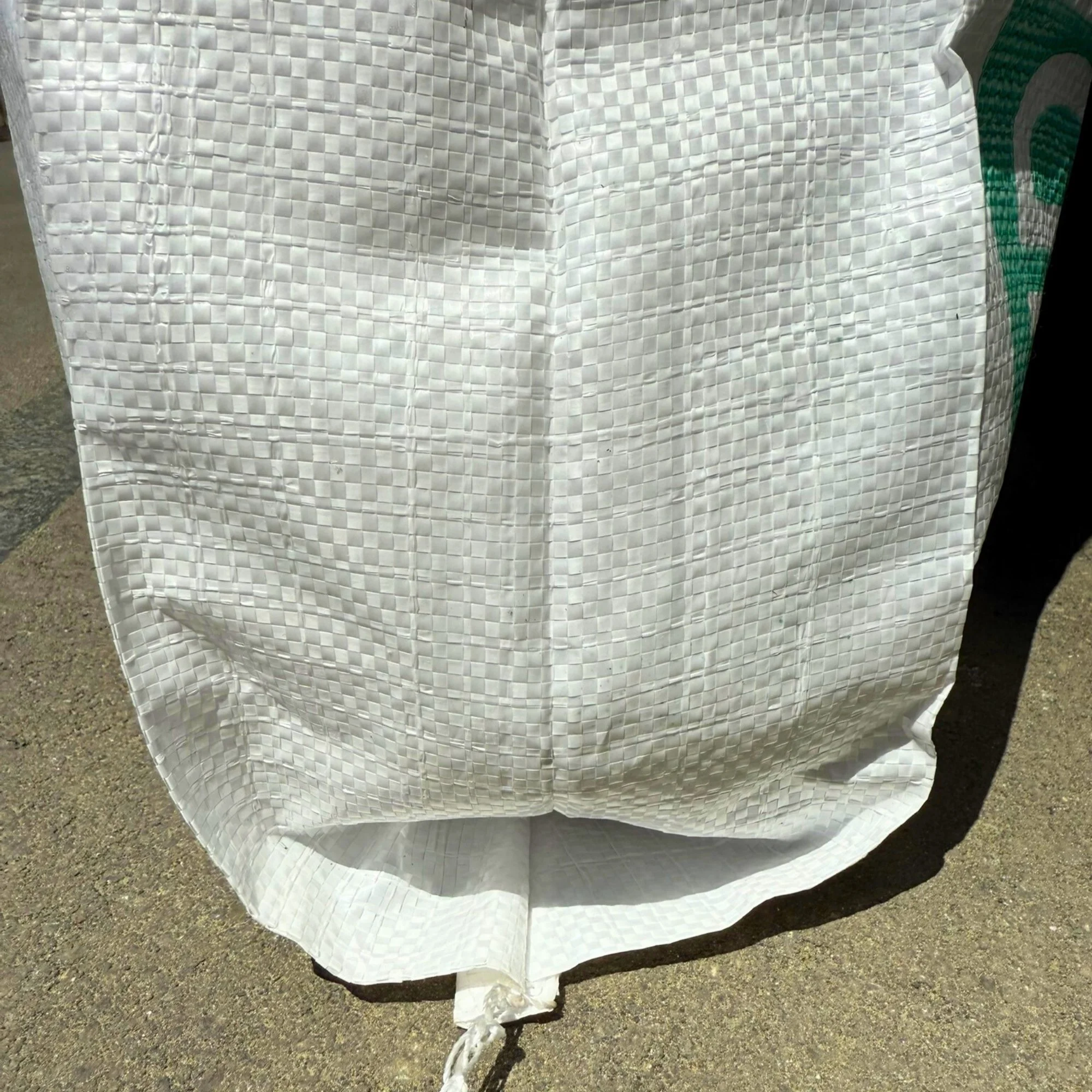 Close-up of a white woven PP bag with flat bottom and gusset placed on asphalt ground.