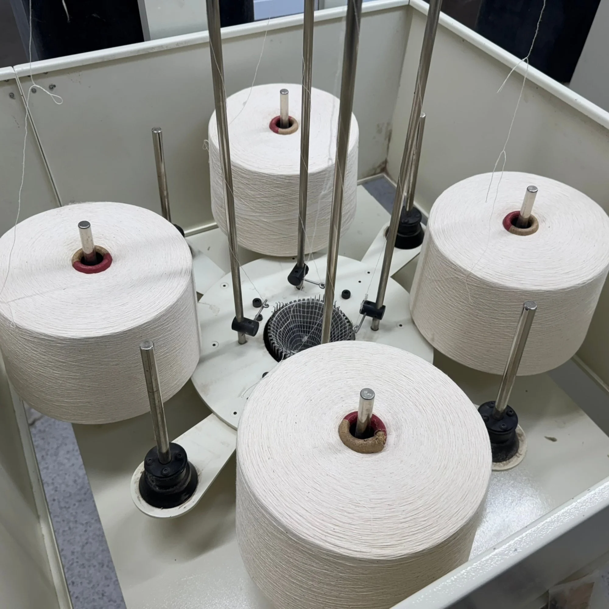 Industrial machine with five large Mussock Saffron Yarn spools of thread mounted on metal rods, used for mussock socking manufacturing or weaving.