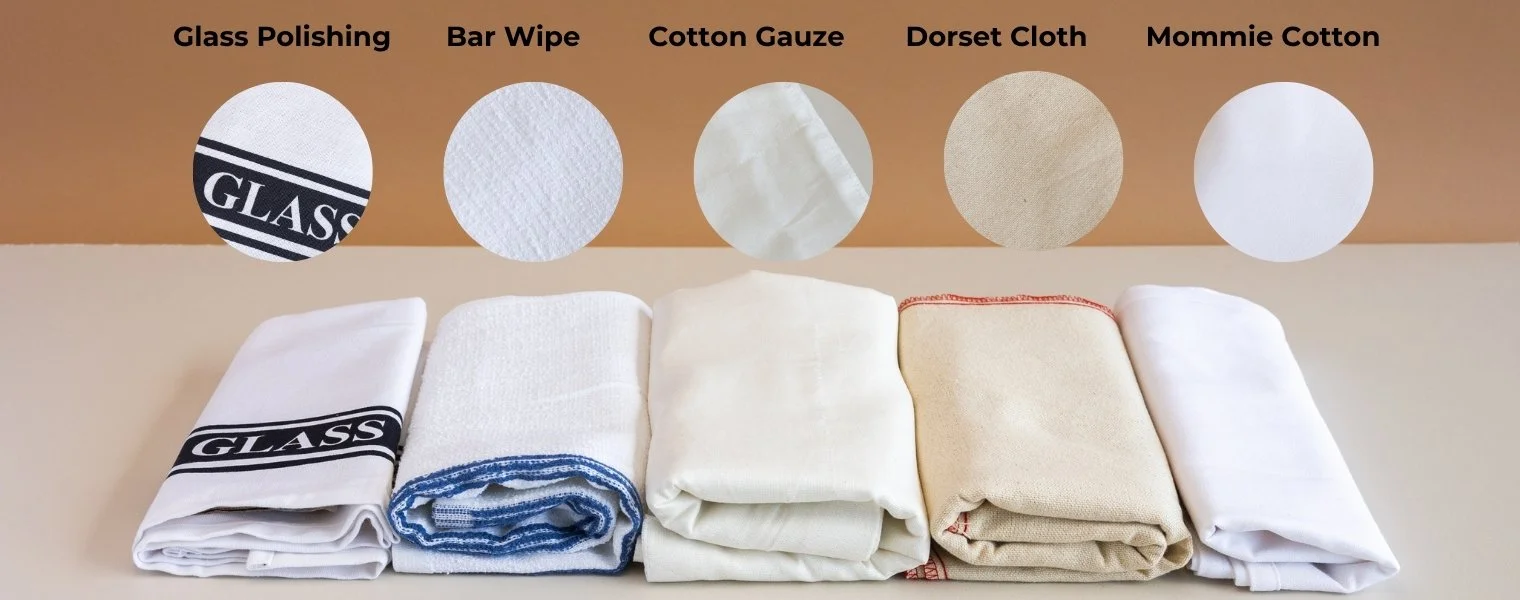 Collection of five folded cleaning cloths with labels above indicating different fabric types: Glass Polishing, Bar Wipe, Cotton Gauze, Dorset Cloth, Mommie Cotton.