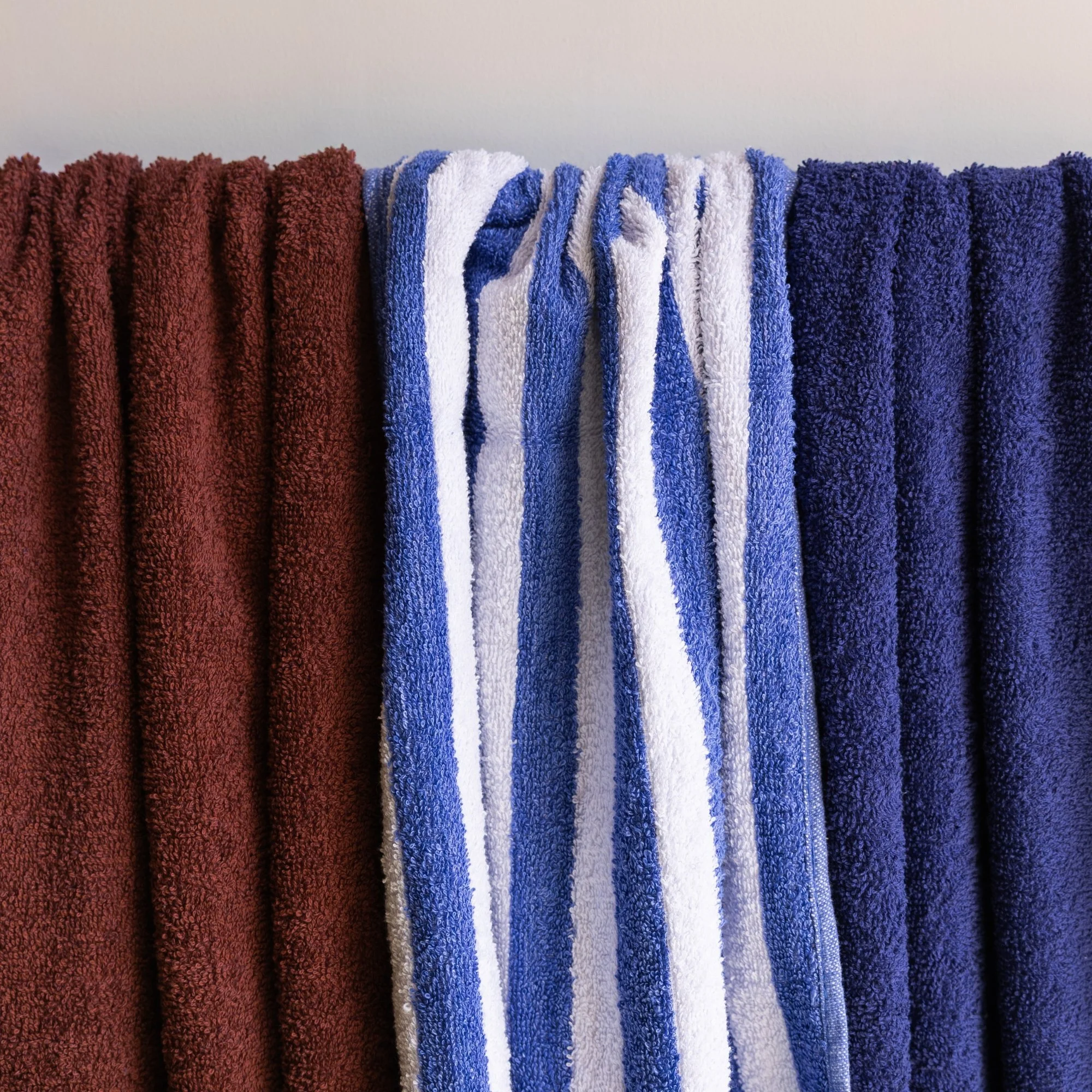 Colorful loop towels hanging on a rail, featuring solid red, striped white and blue, and solid navy blue towels.