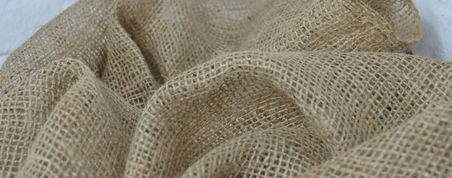 Close-up of beige jute fabric with a rough woven texture, draped in folds.