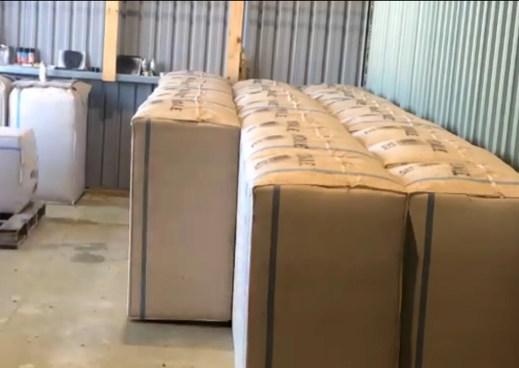 Stack of large cardboard boxes inside a storage shed with metallic walls and a concrete floor.