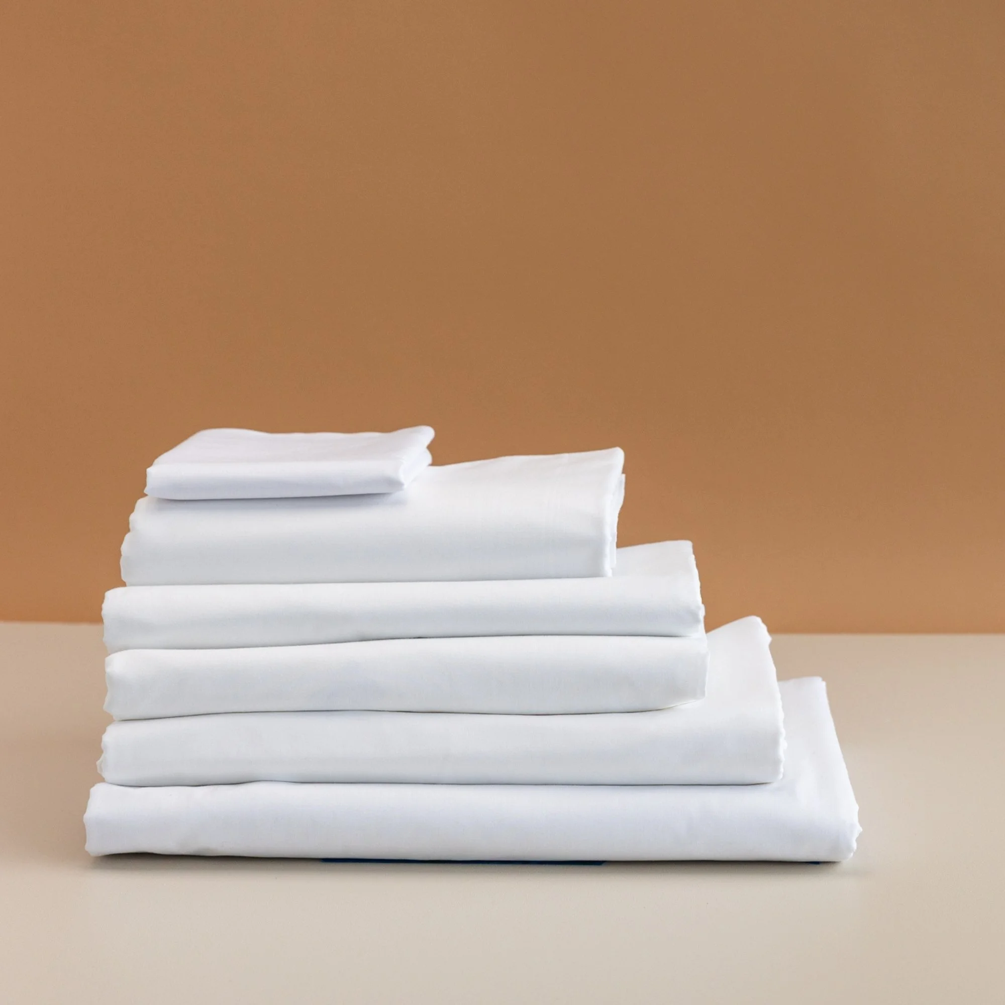 Stack of neatly folded Rutherford 25mm Striped Sheet Set on a beige surface with a brown loose neutral background.