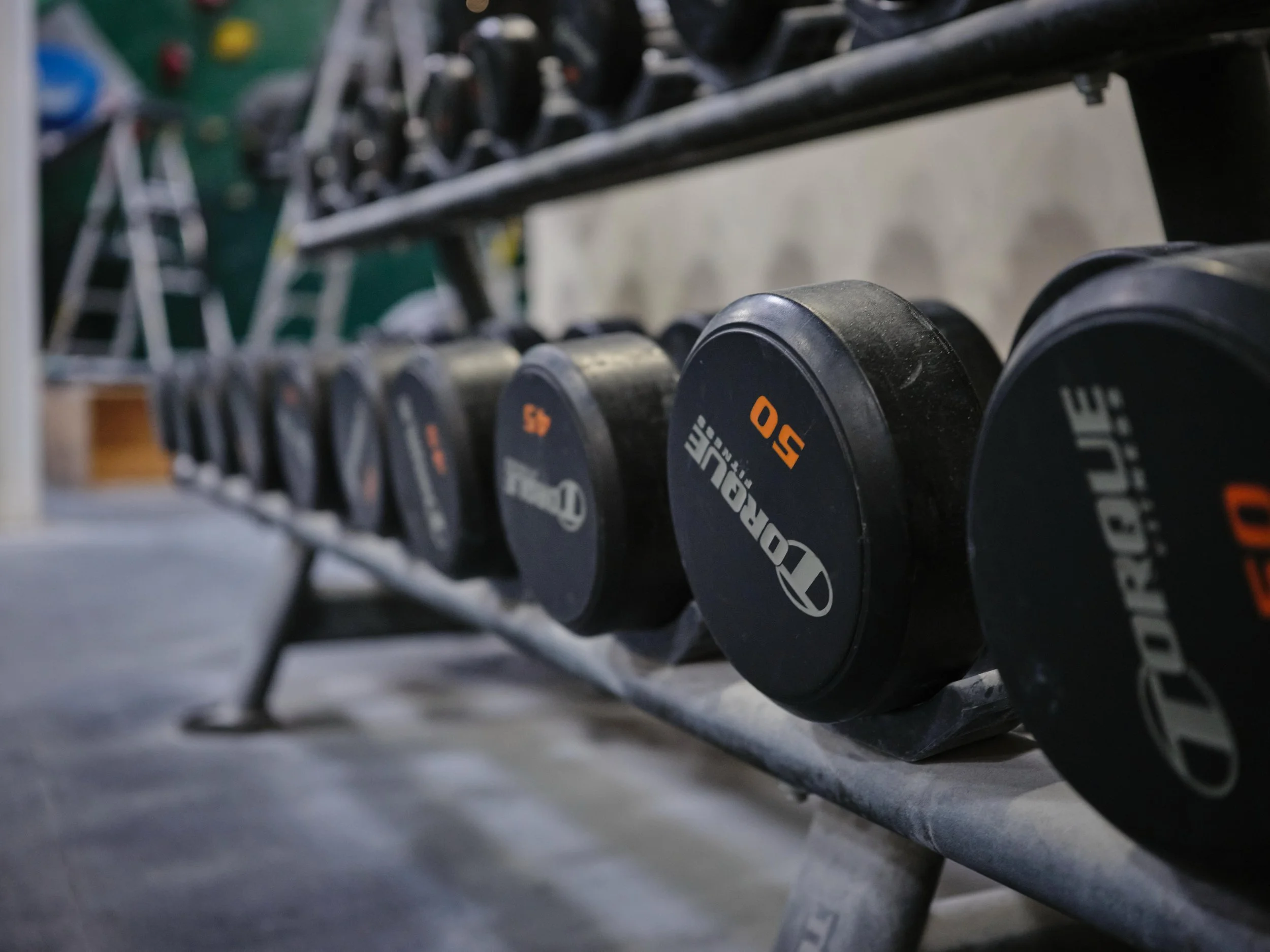 A rack of black dumbbells placed on a metal shelf, with some weight labels visible on the ends.