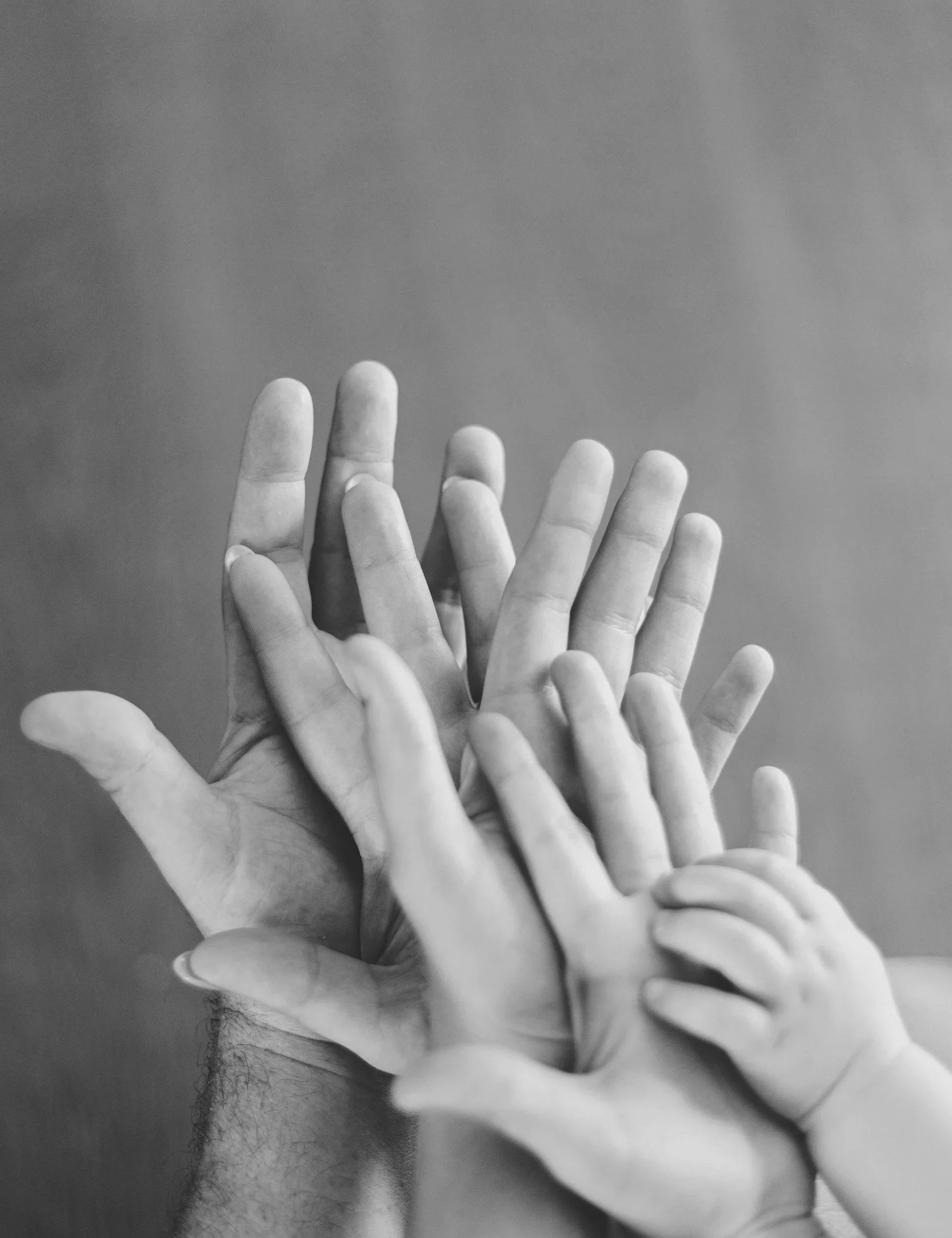 Multiple hands reaching upwards on a person's face, with a gray background.