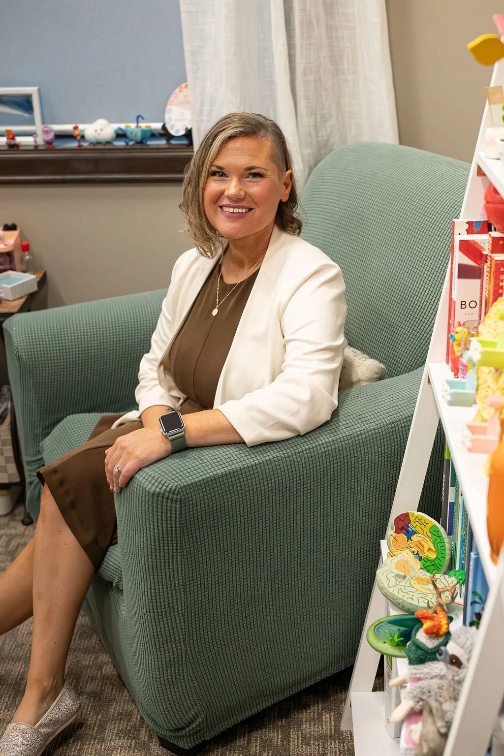 Krysta Winter, counselor at Christian Family Care, seated and smiling in a green armchair in her warm Sioux Falls counseling office lined with books and toys.