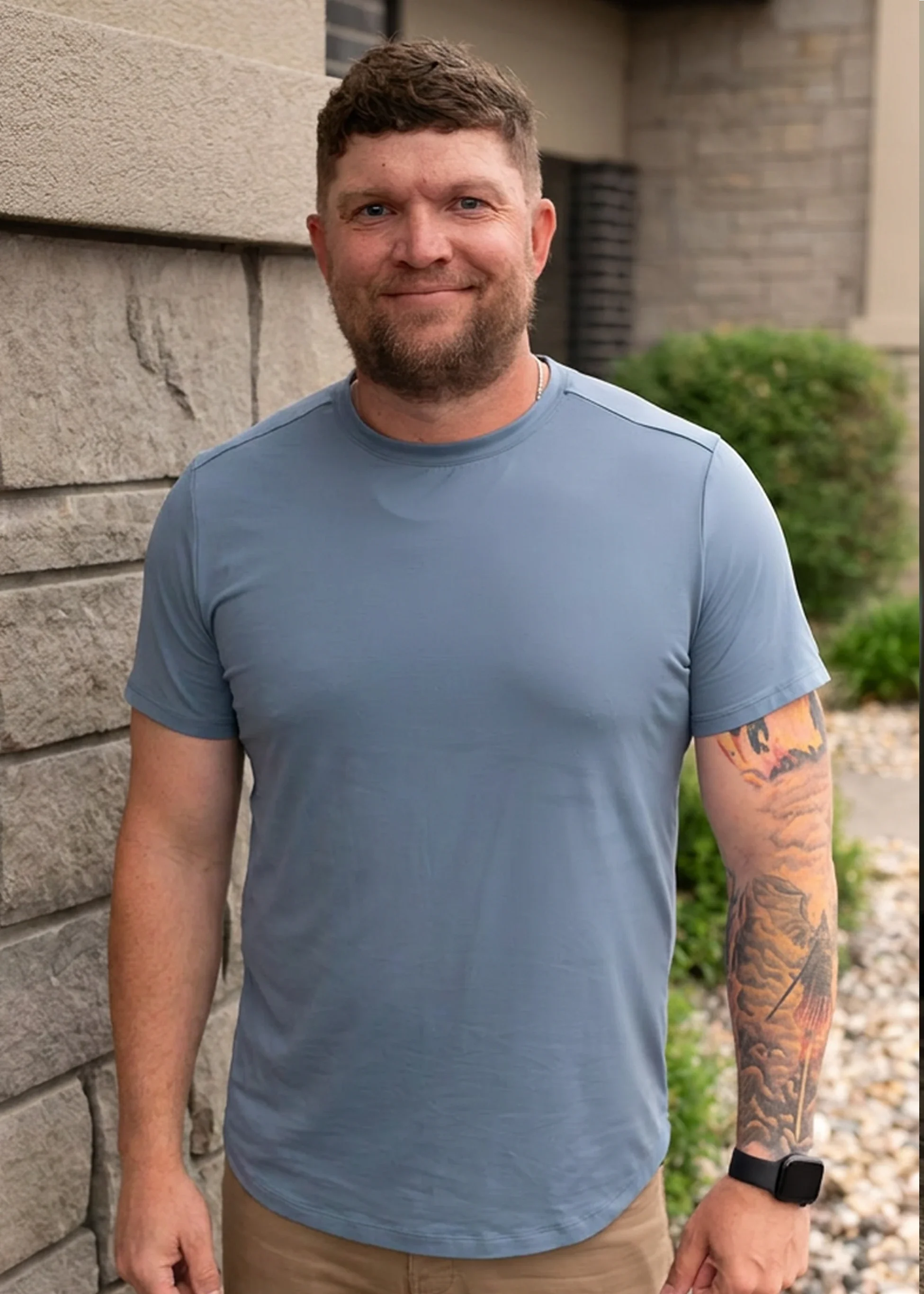 Kyle Winter, Christian men’s mental health coach in Sioux Falls, SD, standing outdoors beside a stone building, wearing a blue shirt and smiling at the camera.