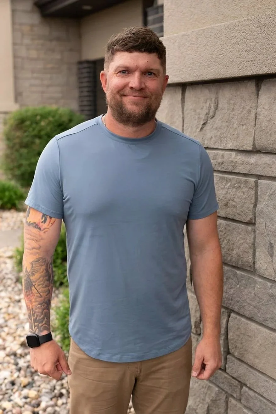 Kyle Winter, Christian men’s mental health coach in Sioux Falls, SD, standing outdoors beside a stone building, wearing a blue shirt and smiling at the camera.