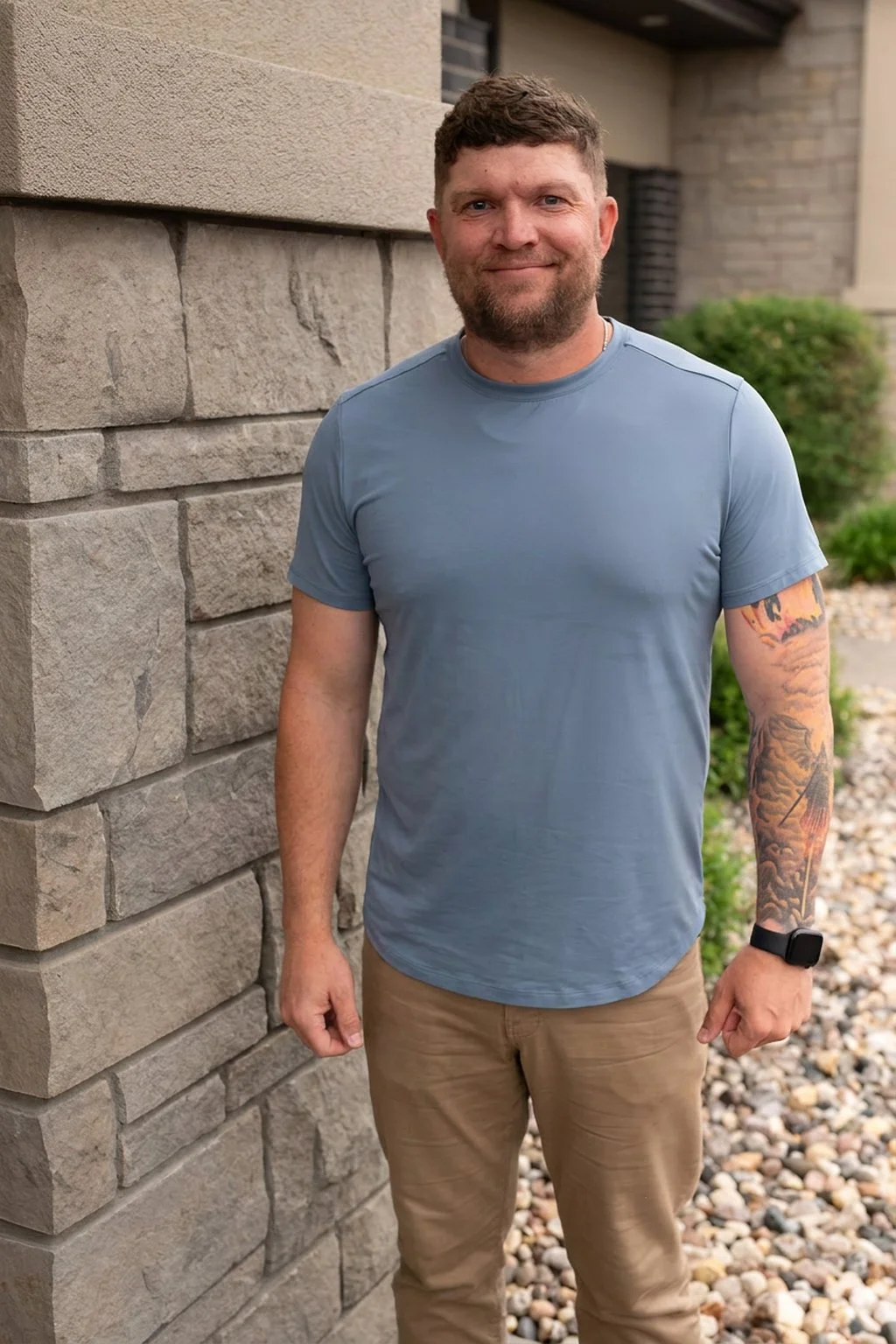 Kyle Winter, Christian men’s mental health coach in Sioux Falls, SD, standing outdoors beside a stone building, wearing a blue shirt and smiling at the camera.
