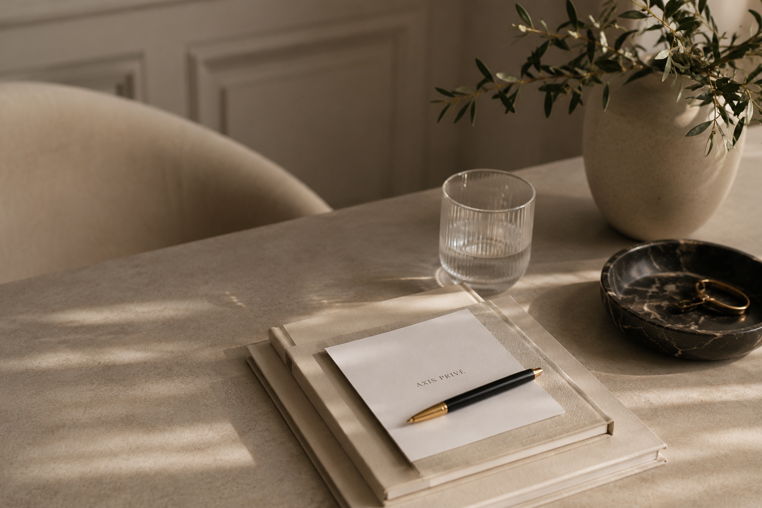 Marble table with a notebook, pen, glass of water, vase, and small decorative bowl in natural light