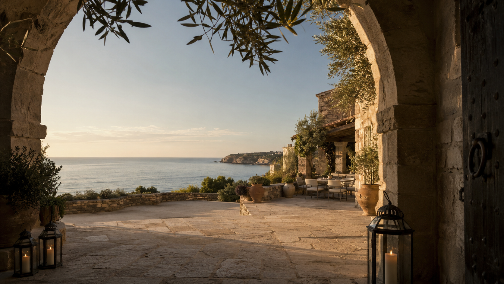 Private stone terrace overlooking the ocean with lanterns, potted plants, and outdoor dining furniture.