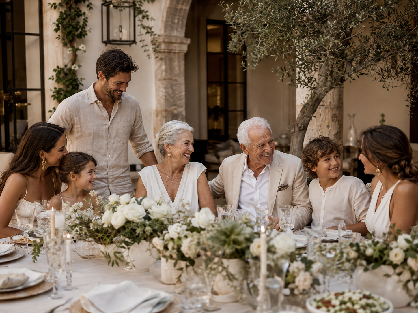 Multi-generational family gathered around an outdoor dining table with flowers, candles, and a warm celebratory setting