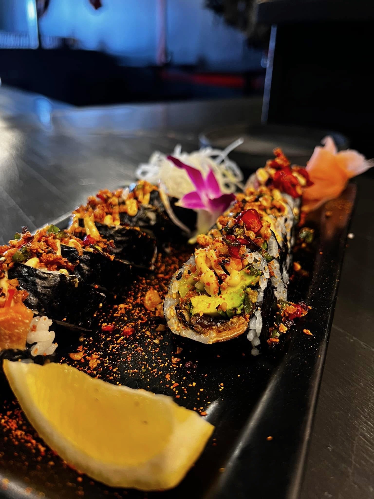 Close-up of assorted sushi rolls garnished with spices and flowers on a black serving platter.
