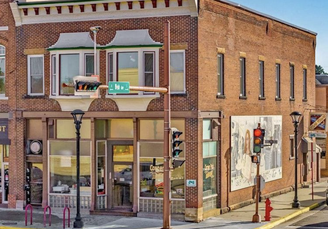 Street corner with brick buildings, traffic lights, street signs, lampposts, and murals on building walls.