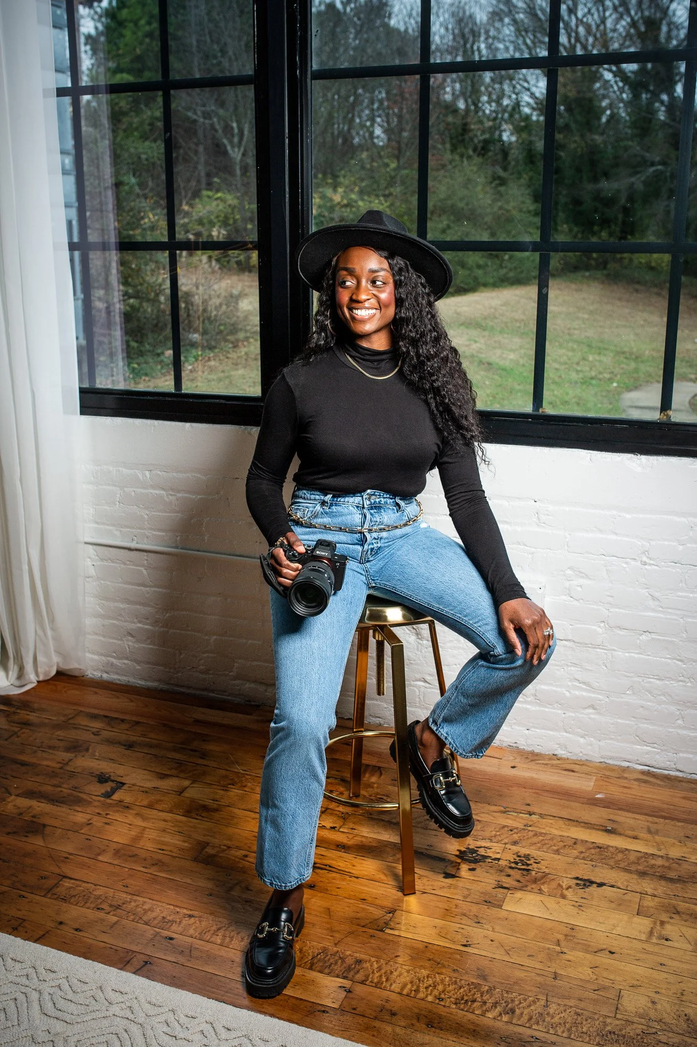 woman in black hat sitting on stool holding camera