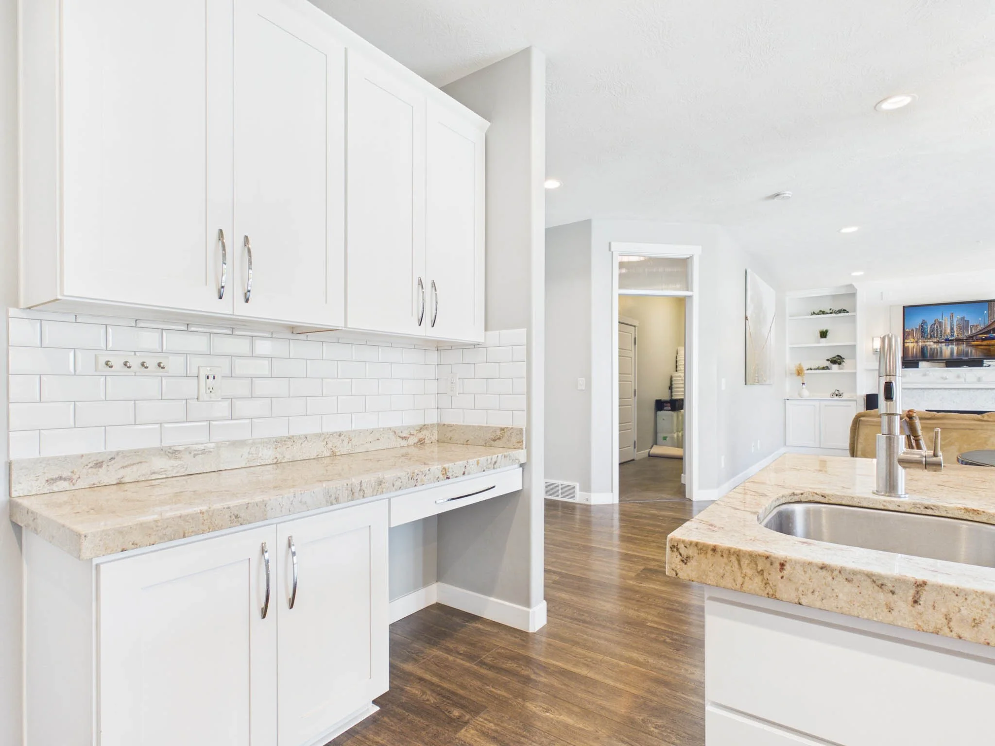 Modern kitchen with white cabinets, granite countertops, white subway tile backsplash, and hardwood floors.