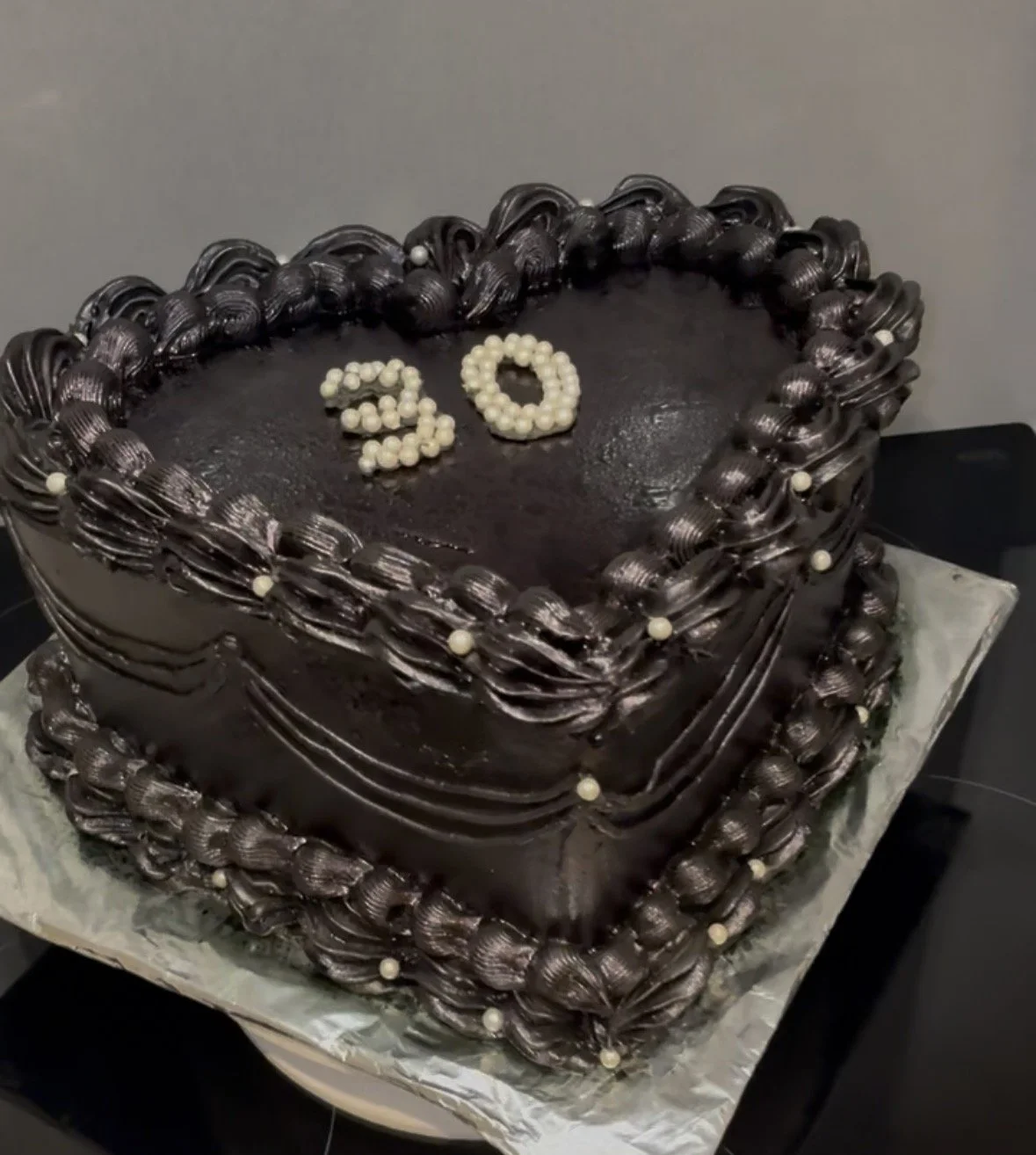 A heart-shaped chocolate cake decorated with glossy chocolate frosting and white pearls, with the number 30 on top made of white pearls.