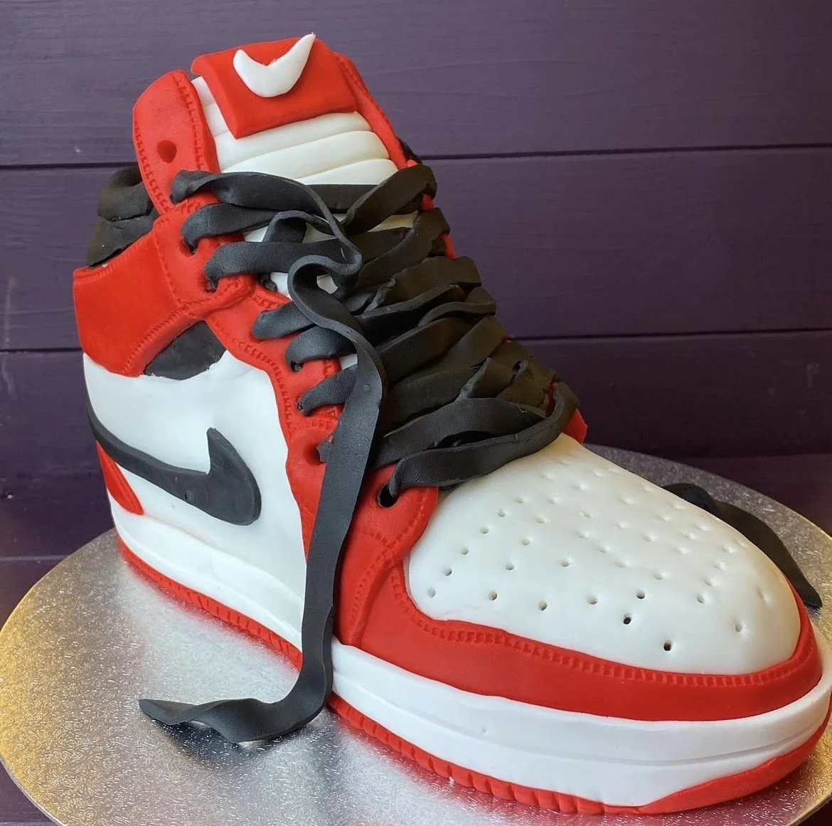 A cake designed to look like a sneaker, resembling a Nike Air Jordan 1, with red, white, black, and gray fondant details.