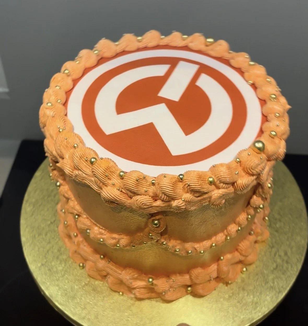 Cake with orange frosting and gold accents, featuring the logo of the political party 'Yedisi' on top.