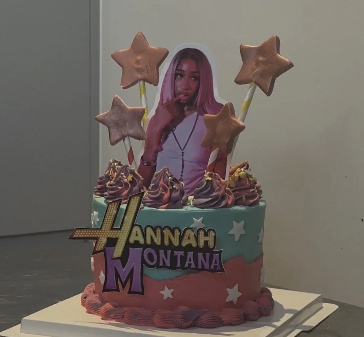 Celebration cake with a photo of Hannah Montana, colorful icing, star-shaped cookies, and decorative signs with Hannah Montana's name.