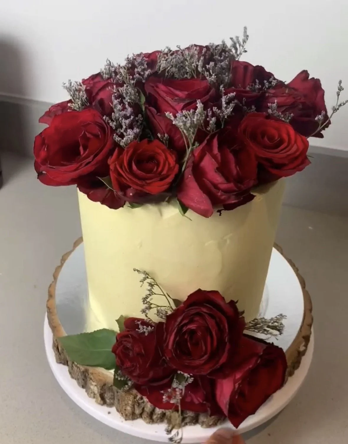 A wedding cake decorated with red roses and white baby's breath flowers, with a wooden border around the base.