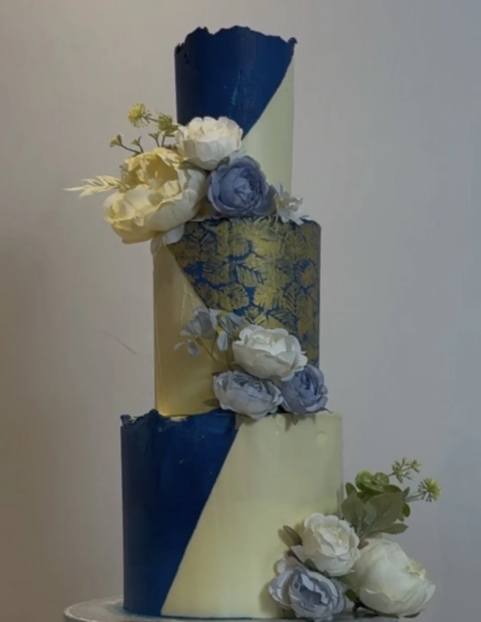 A tall, multi-layered cake decorated with blue, white, and gold floral accents.