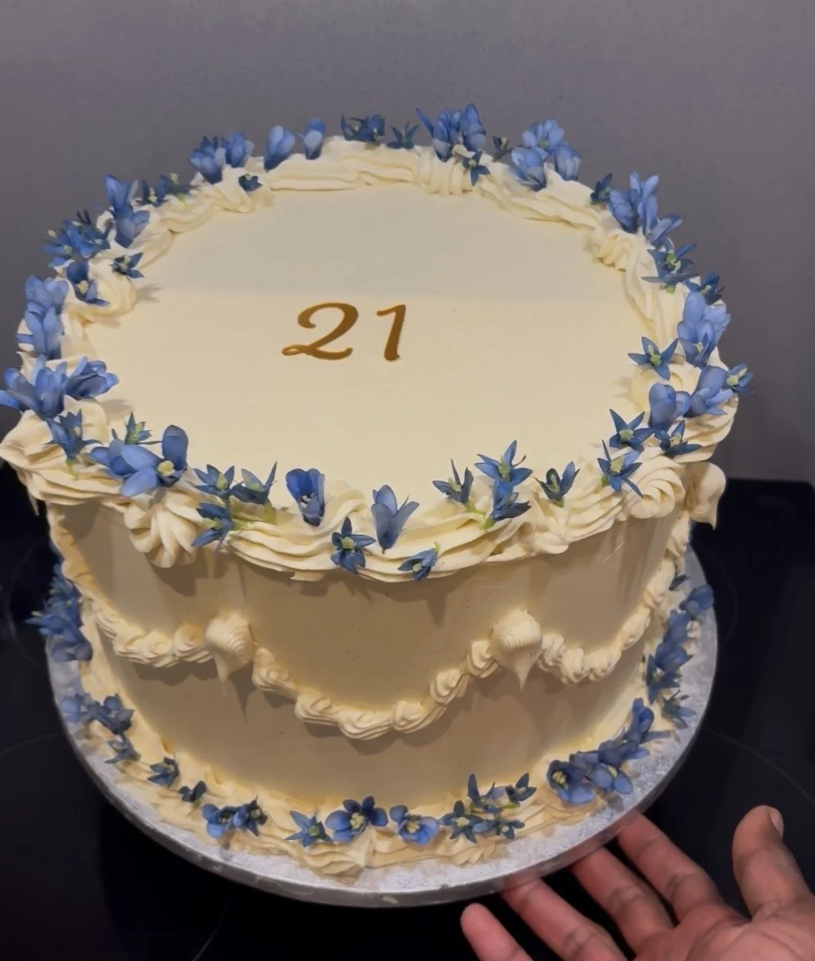 A round birthday cake decorated with cream and blue flowers, with the number 21 written in the center.