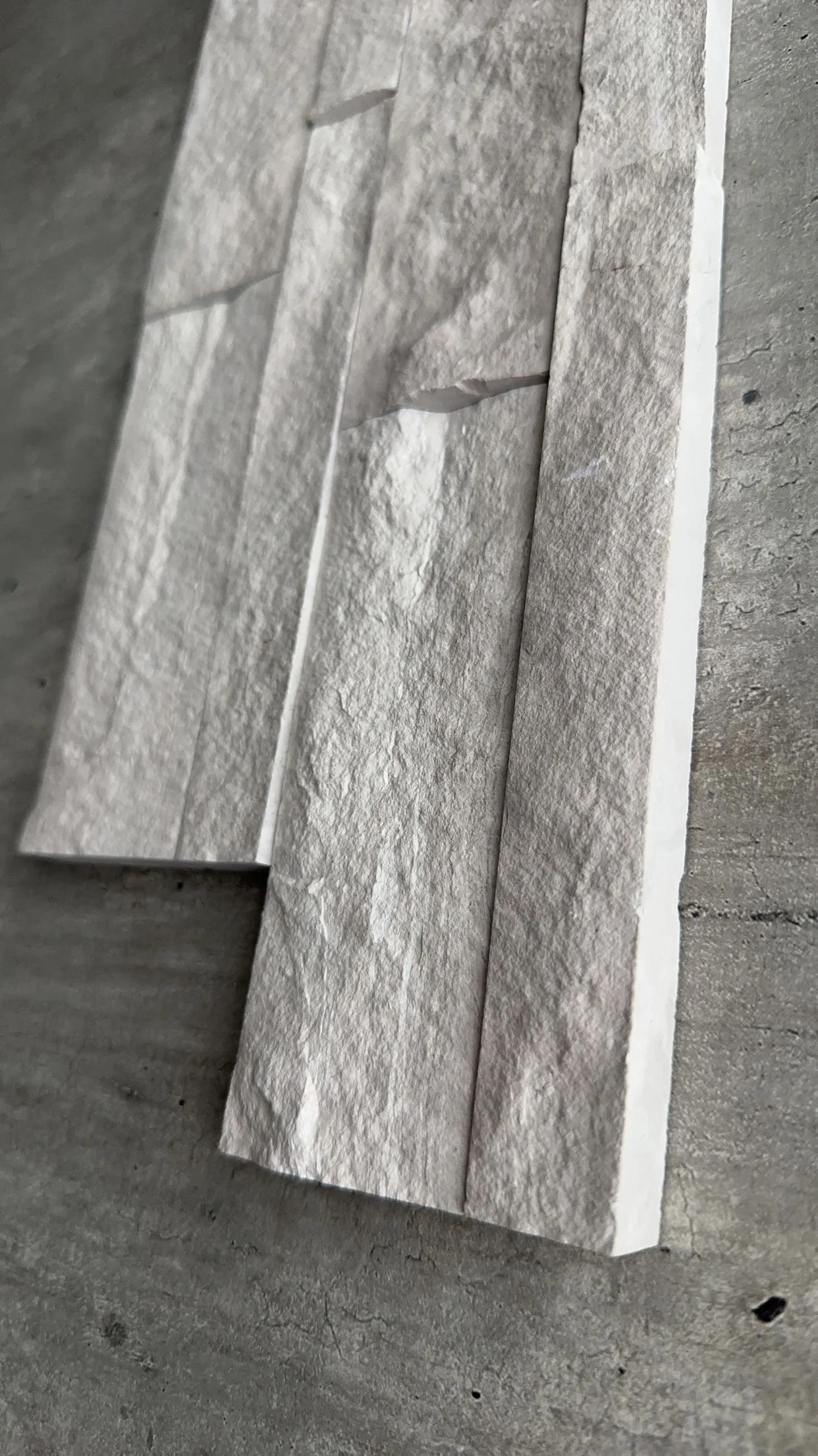 Close-up of various gray textured stone tiles stacked on a concrete surface.